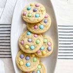 Five Easter M&M Cookies topped with pastel-colored candy-coated chocolates, arranged on a white oval plate.