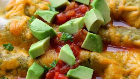 A glass dish filled with enchiladas topped with melted cheese, diced avocado, salsa, and chopped cilantro—perfect for Spring 5 Ingredient Dinners.
