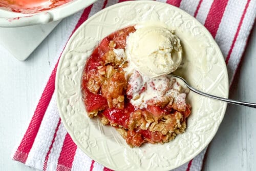 Closeup view of white bowl with Strawberry Crisp and ice cream.