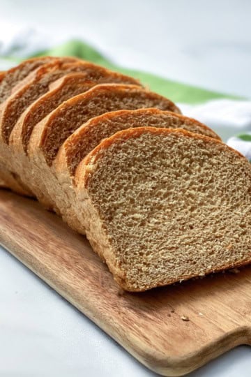 Sliced whole wheat bread made in two loaves with a striped linen in the background.