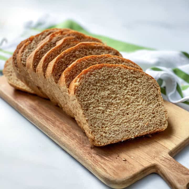 Sliced whole wheat bread made in two loaves with a striped linen in the background.