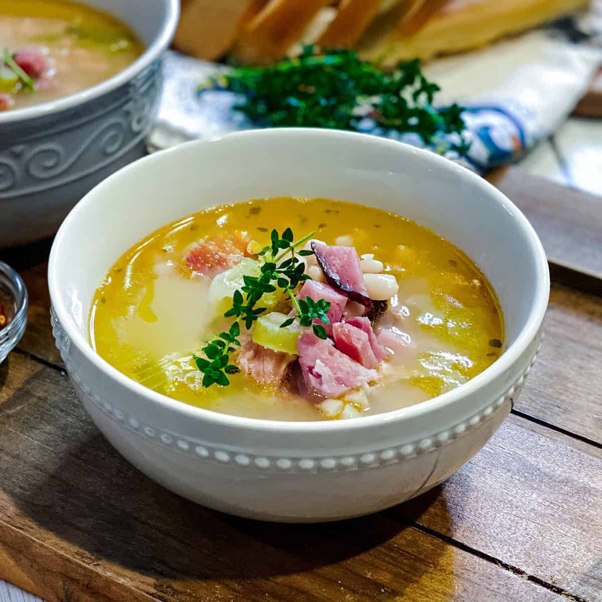Bowl of Ham Bone White Bean Soup topped with chopped ham and fresh thyme leaves resting on a wooden serving board.