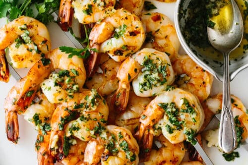 Grilled shrimp skewers garnished with chopped herbs, served with lemon slices, fresh parsley, and a small bowl of herb sauce-perfect for your Memorial Day recipes collection.