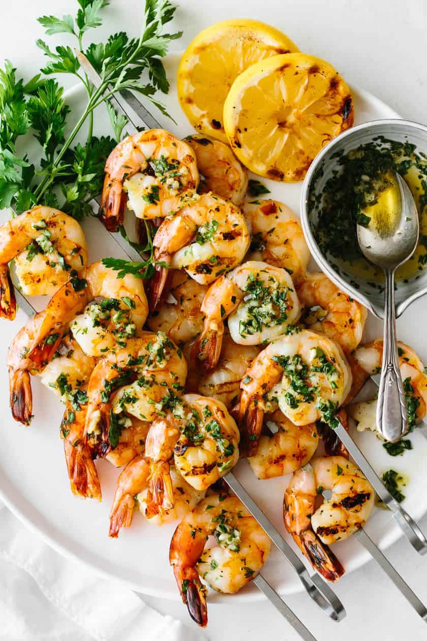 Grilled shrimp skewers garnished with chopped herbs, served with lemon slices, fresh parsley, and a small bowl of herb sauce-perfect for your Memorial Day recipes collection.