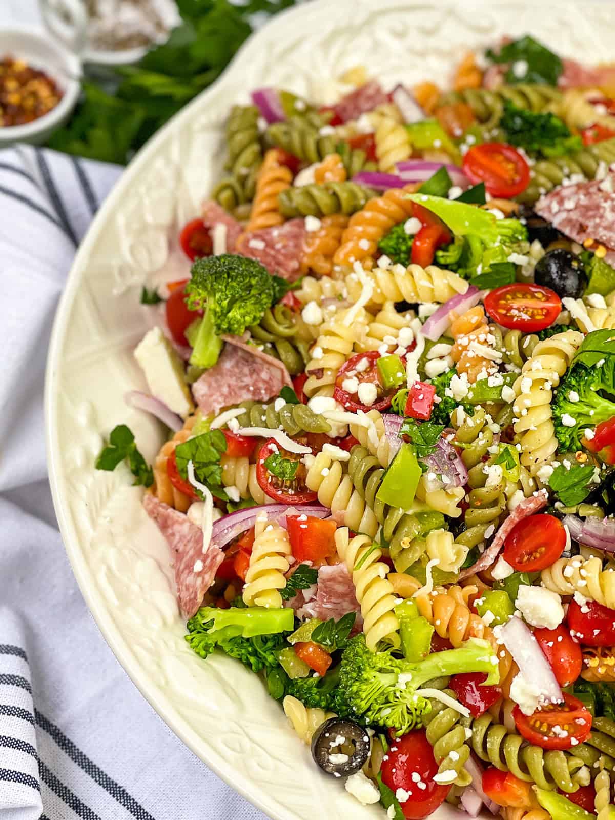 Close-up of summer pasta salad with rotini, broccoli, tomatoes, peppers, olives, salami, and feta.