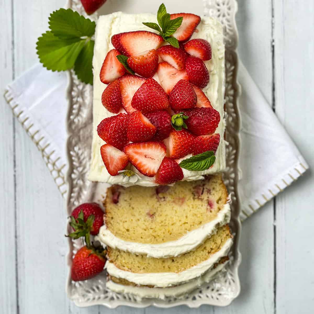 Rectangular strawberry cake with white frosting, topped with fresh strawberries and mint.