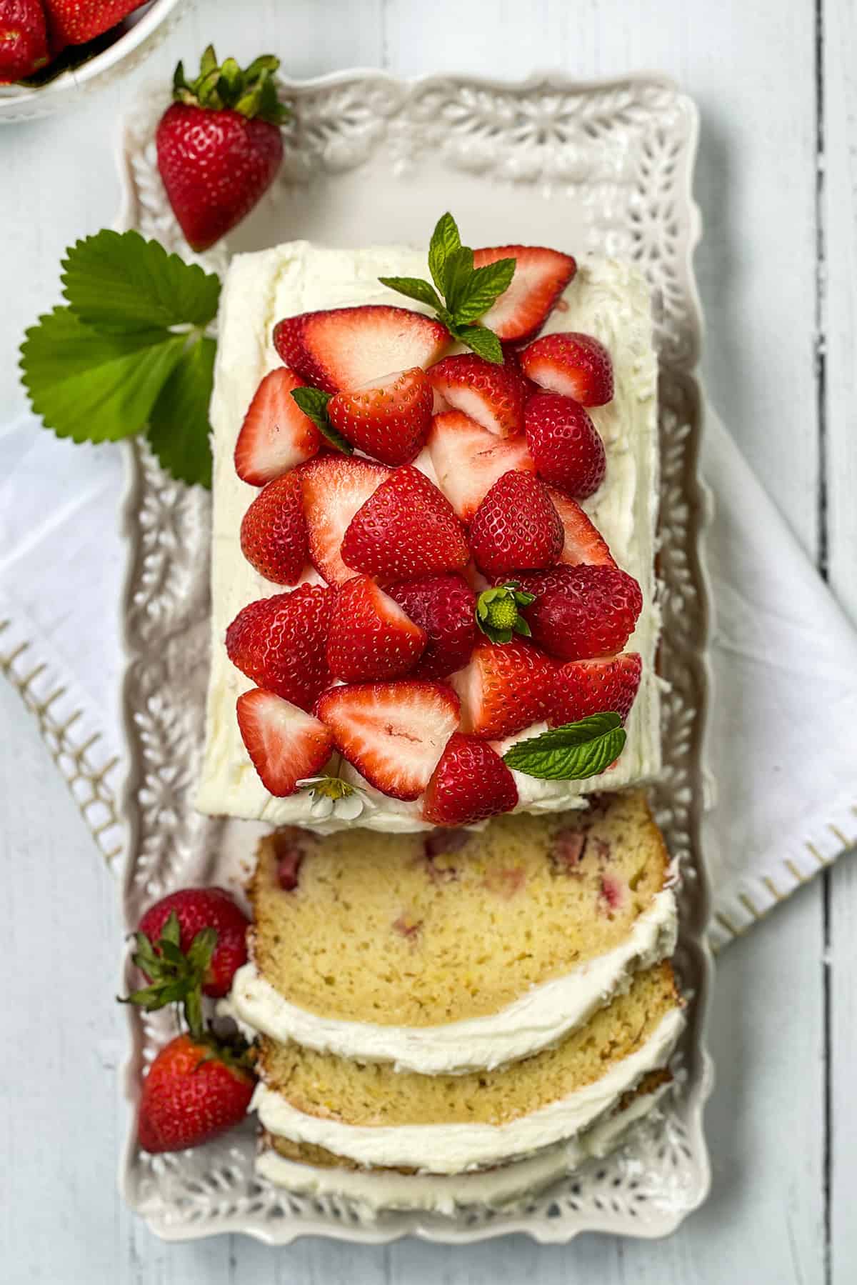 A rectangular strawberry cake with frosting, topped with sliced strawberries and mint. 
