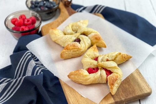 Two berry pinwheel pastries on a sheet of parchment paper with fresh raspberries and blueberries
