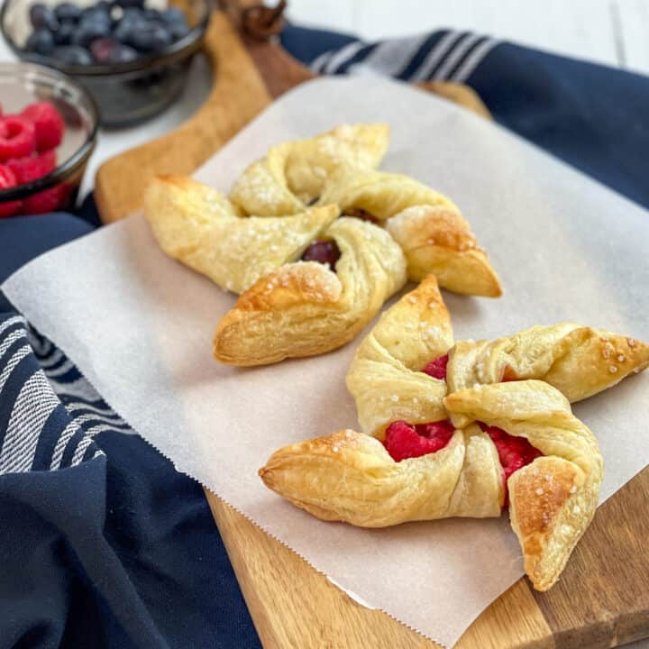 Two berry pinwheel pastries on a sheet of parchment paper with fresh raspberries and blueberries