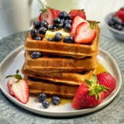 Stack of whole wheat waffles topped with fresh berries on a white plate.