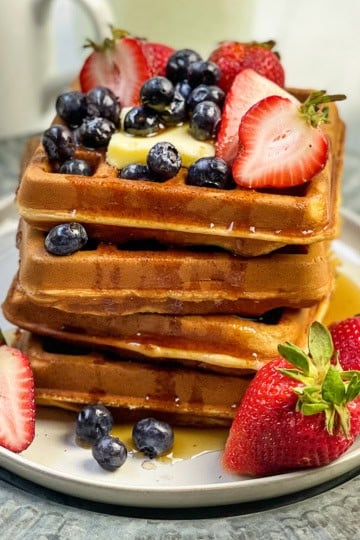 Stack of whole wheat waffles topped with fresh berries on a white plate.