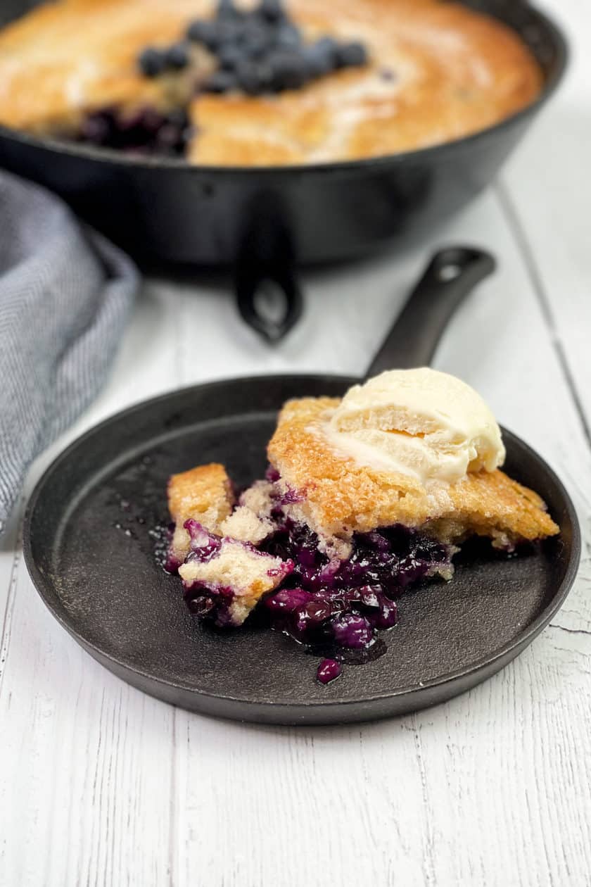 Slice of Blueberry Cobbler with Vanilla Ice Cream on a skillet shaped serving dish.