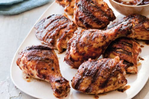 Side view of BBQ chicken pieces on a white plate on a rustic wooden background.
