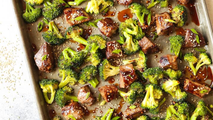 A perfect option for June sheet pan dinners, this baking sheet features cooked broccoli florets and beef pieces, garnished with sesame seeds and sauce.