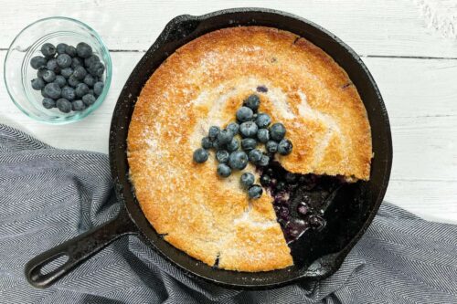 Blueberry Cobbler in a cast iron skillet with slice missing