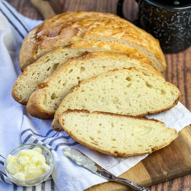 Sliced Dutch Oven Camp Bread on a wooden cutting board with a blue and white towel.