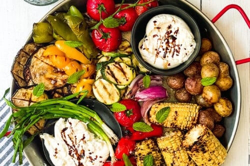 Top view of Grilled Vegetables Platter with bowls of burrato cheese on a white background.