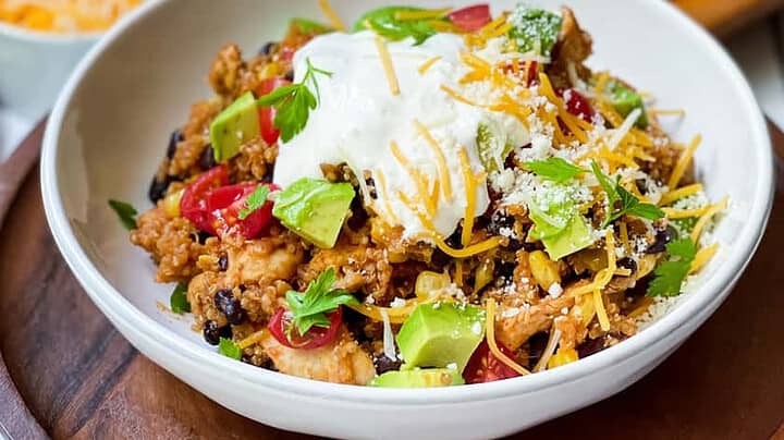 Side view of Instant Pot Chicken Enchilada Quinoa Casserole bowl with Instant Pot in the background.