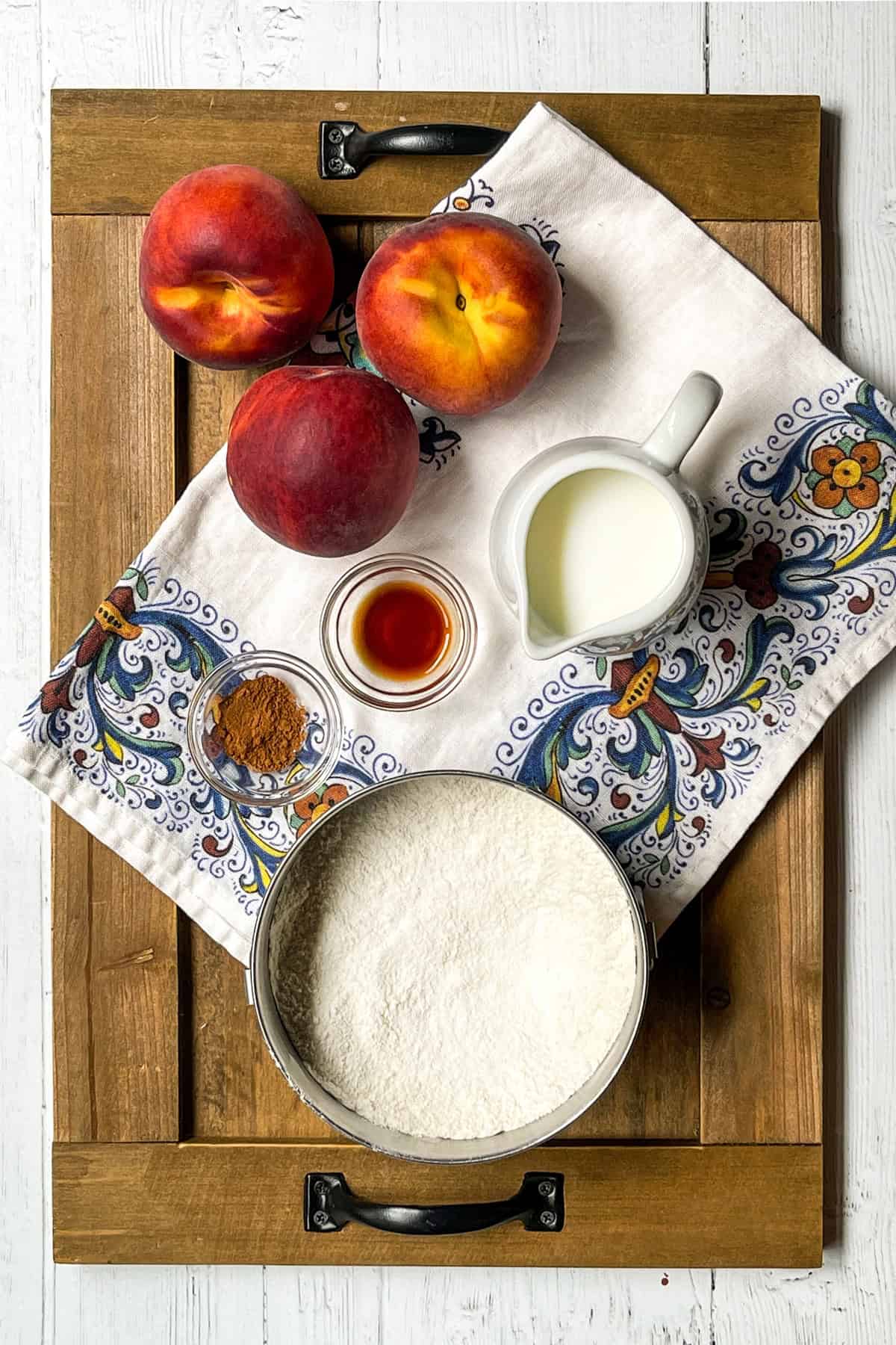 Cobbler ingredients of flour, milk, spices, fresh peaches and flour on a wooden board.