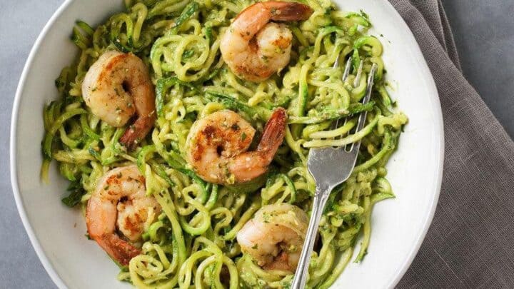 A white bowl with zucchini noodles, grilled shrimp, and a creamy green sauce sits on a gray napkin with a fork—perfect for fresh and easy summer skillet dinners.