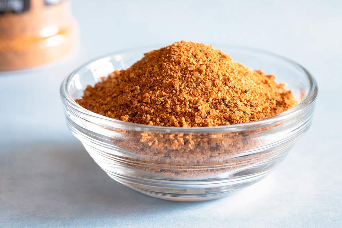 A small clear glass bowl filled with a homemade dry rub recipe blend, ideal for any easy dry rub recipe, sits on a light blue surface.