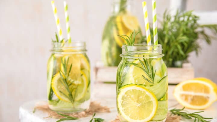 Glass jars of Herb Lemon Water with slices of cucumber, lemon, and fresh herbs