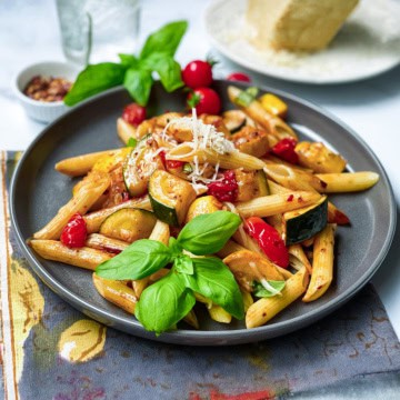 Zucchini pasta with tomatoes on a serving plate with fresh basil.