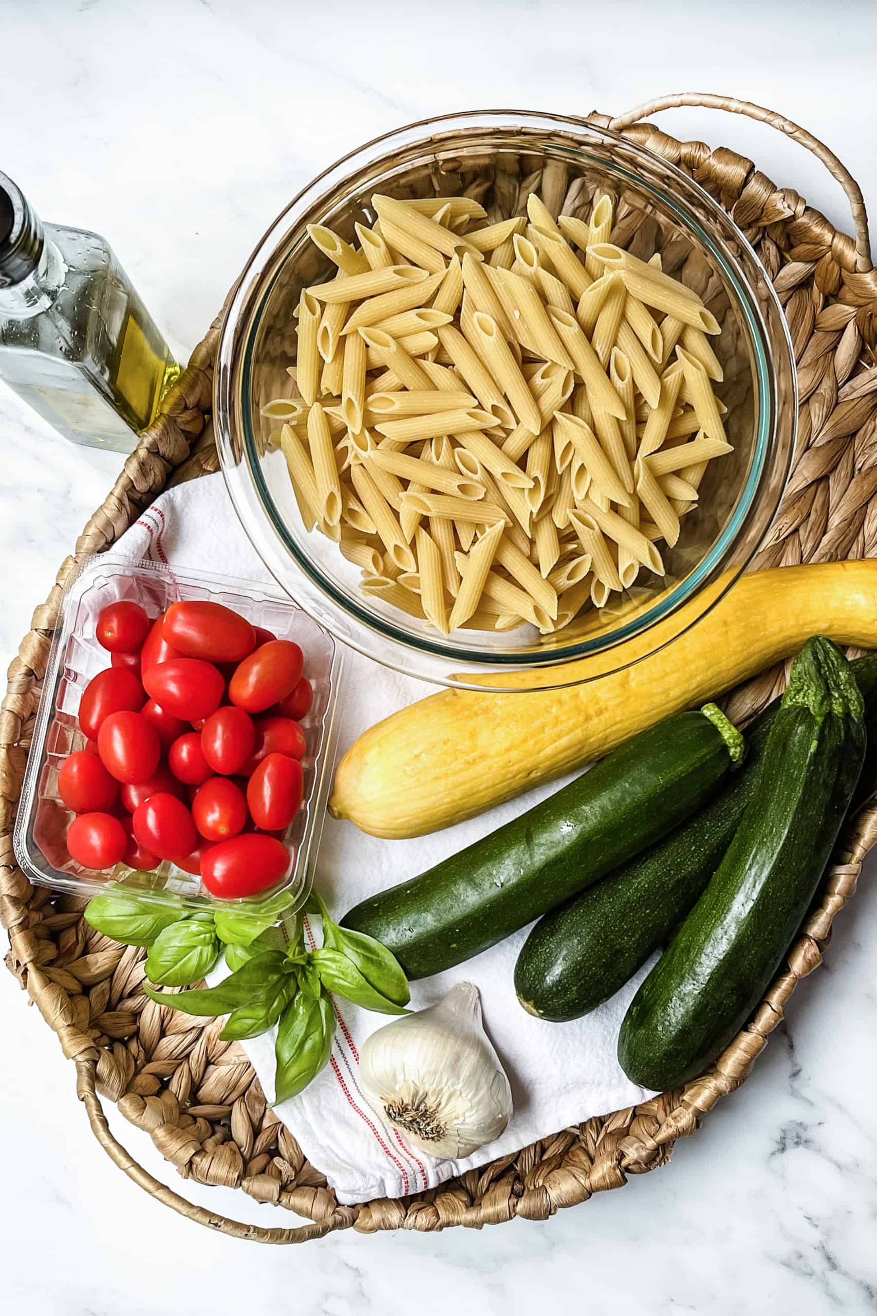 Ingredients for zucchini pasta including dry pasta, cherry tomatoes, zucchini, summer squash, fresh basil and garlic.