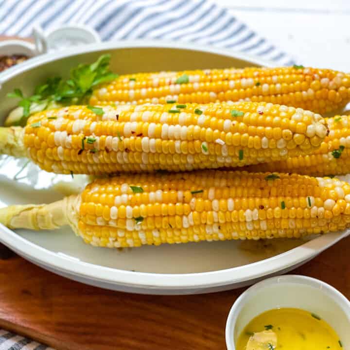 Foil packet grilled corn on the cob in a casserole dish with melted butter and fresh herbs
