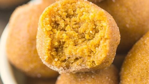 Five delicious oat-topped muffins and two empty baking cups are arranged in a wooden tray lined with burlap fabric, set on a dark wooden surface.