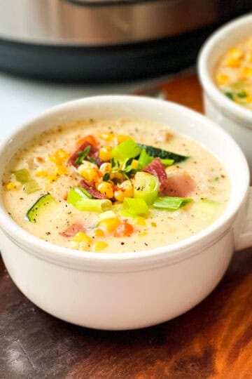 Two bowls of Zucchini Corn Chowder garnished with chopped green onions with a spoon resting nearby.