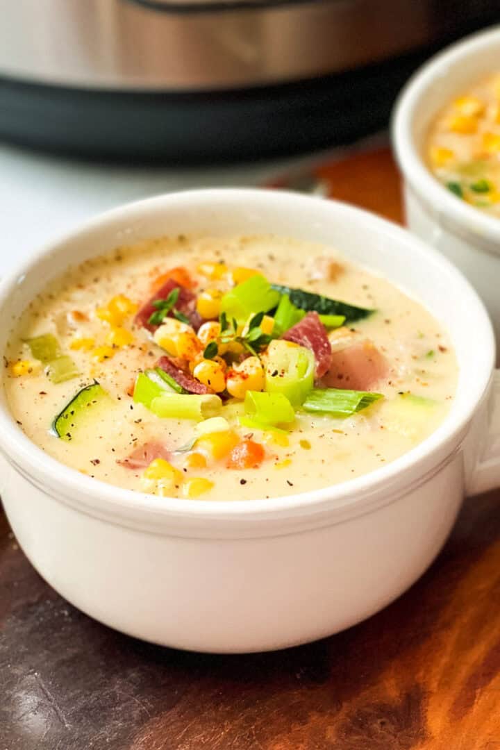 Two bowls of Zucchini Corn Chowder garnished with chopped green onions with a spoon resting nearby.
