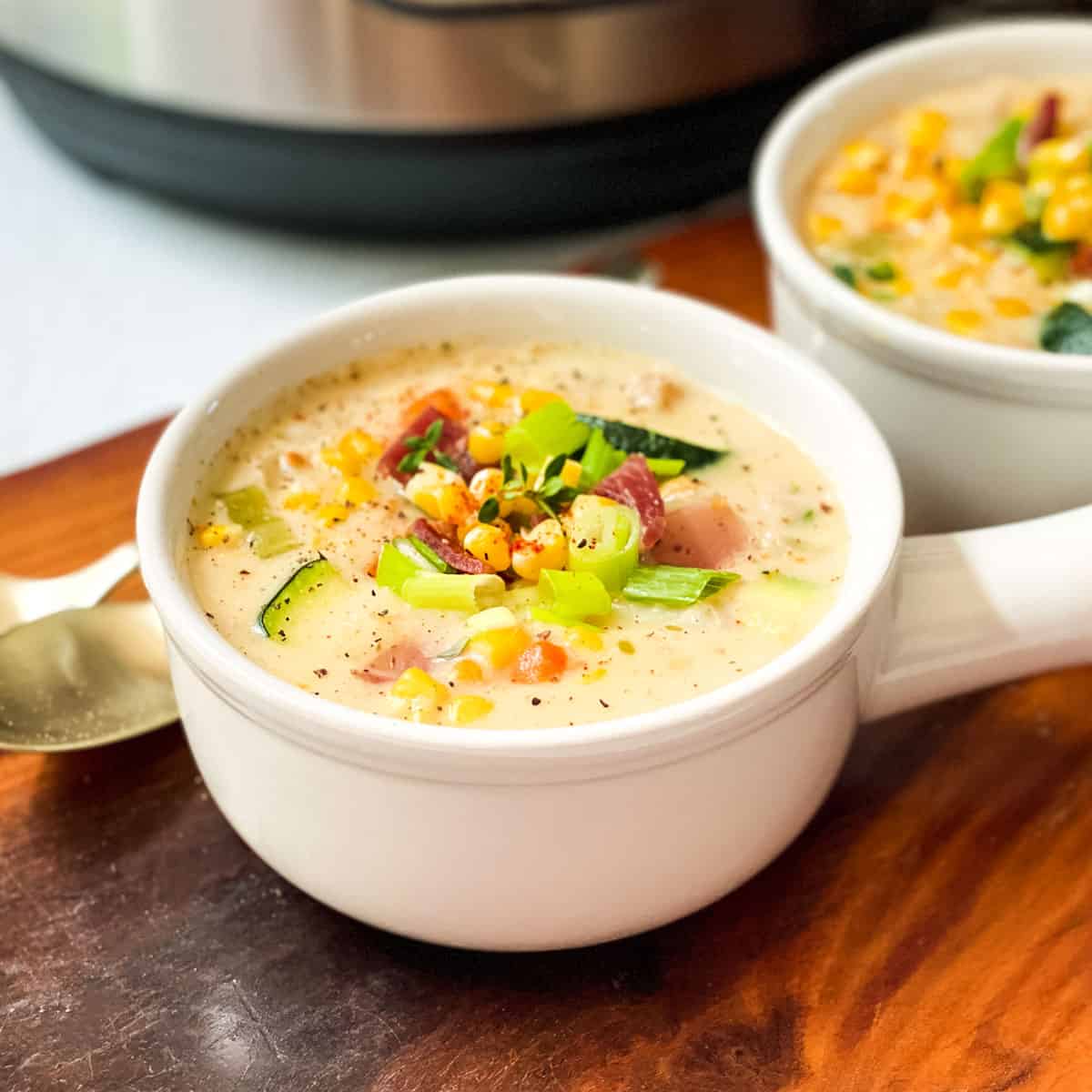 Two bowls of Zucchini Corn Chowder garnished with chopped green onions with a spoon resting nearby.