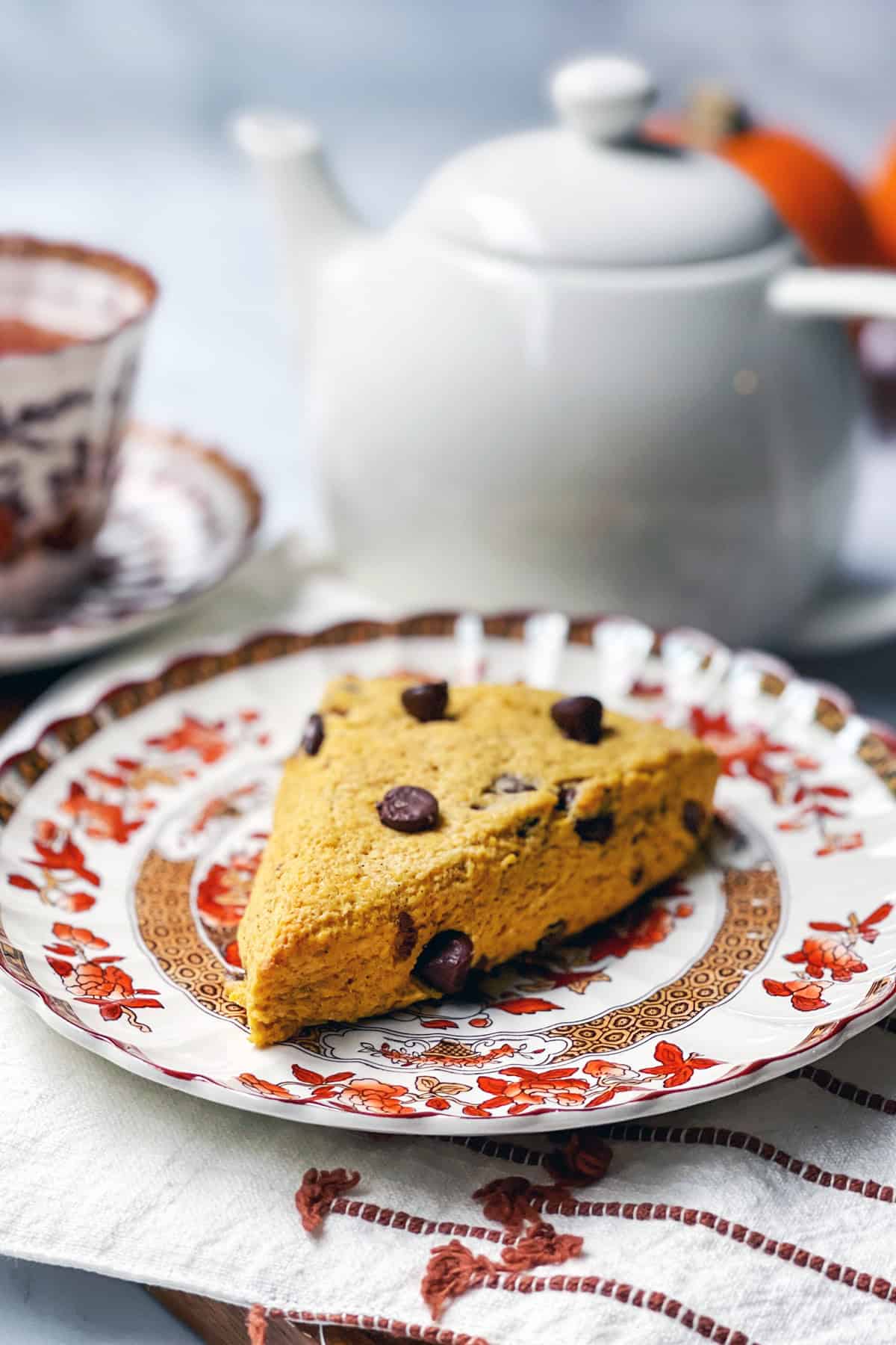 Pumpkin chocolate chip scone on a plate to serve for tea time with a teacup in the background.