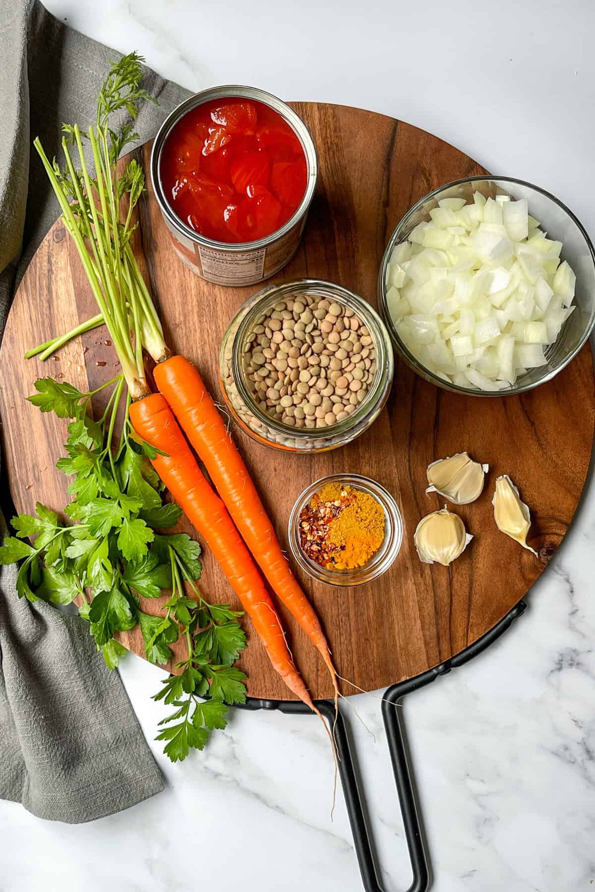 Ingredients for Curry Lentil Soup on a round wood board including carrots, lentils, garlic, spices, onions, and fresh herbs.
