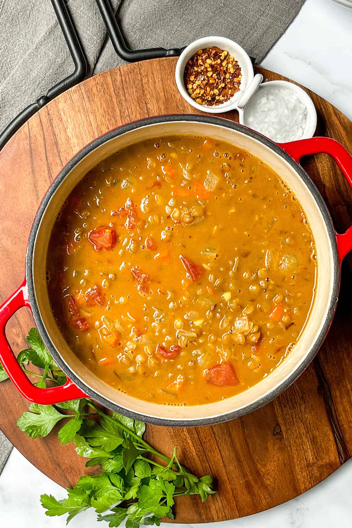 Large pot of lentil soup resting on a wooden board cooling.