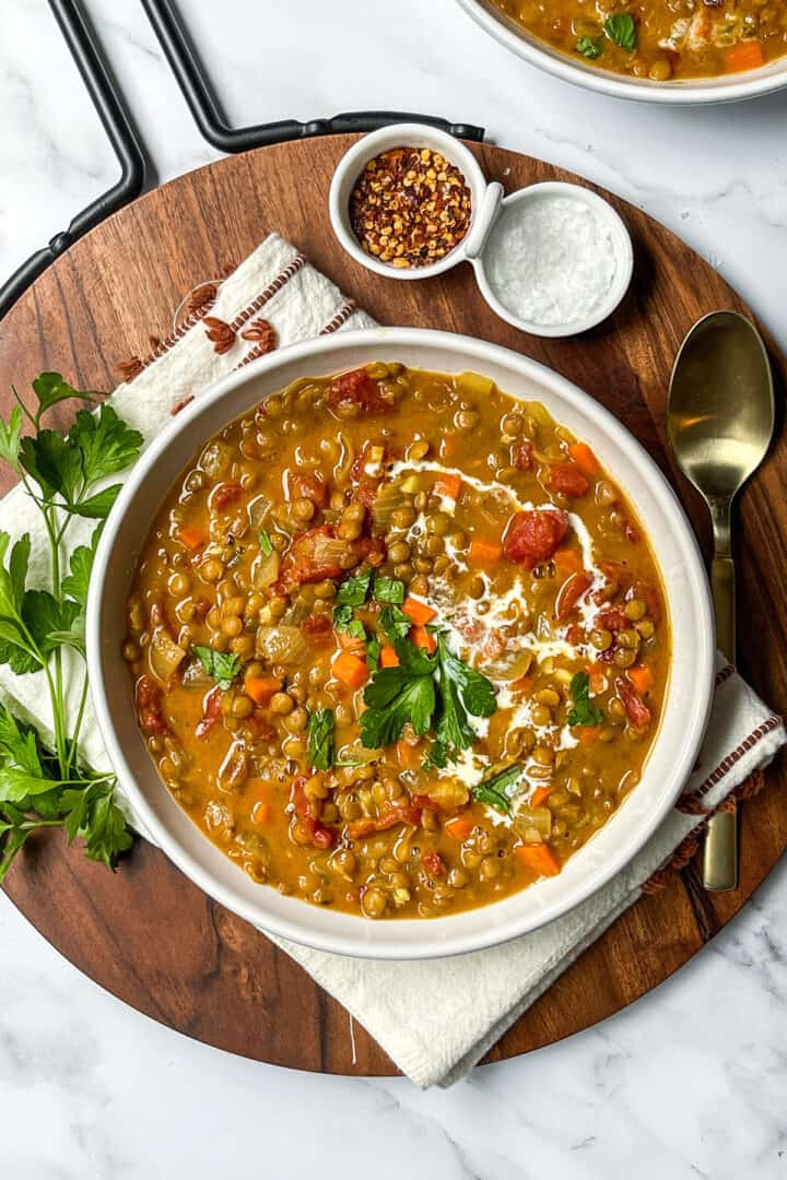 Bowl of curry lentil soup with coconut milk swirls and fresh herbs as garnish.