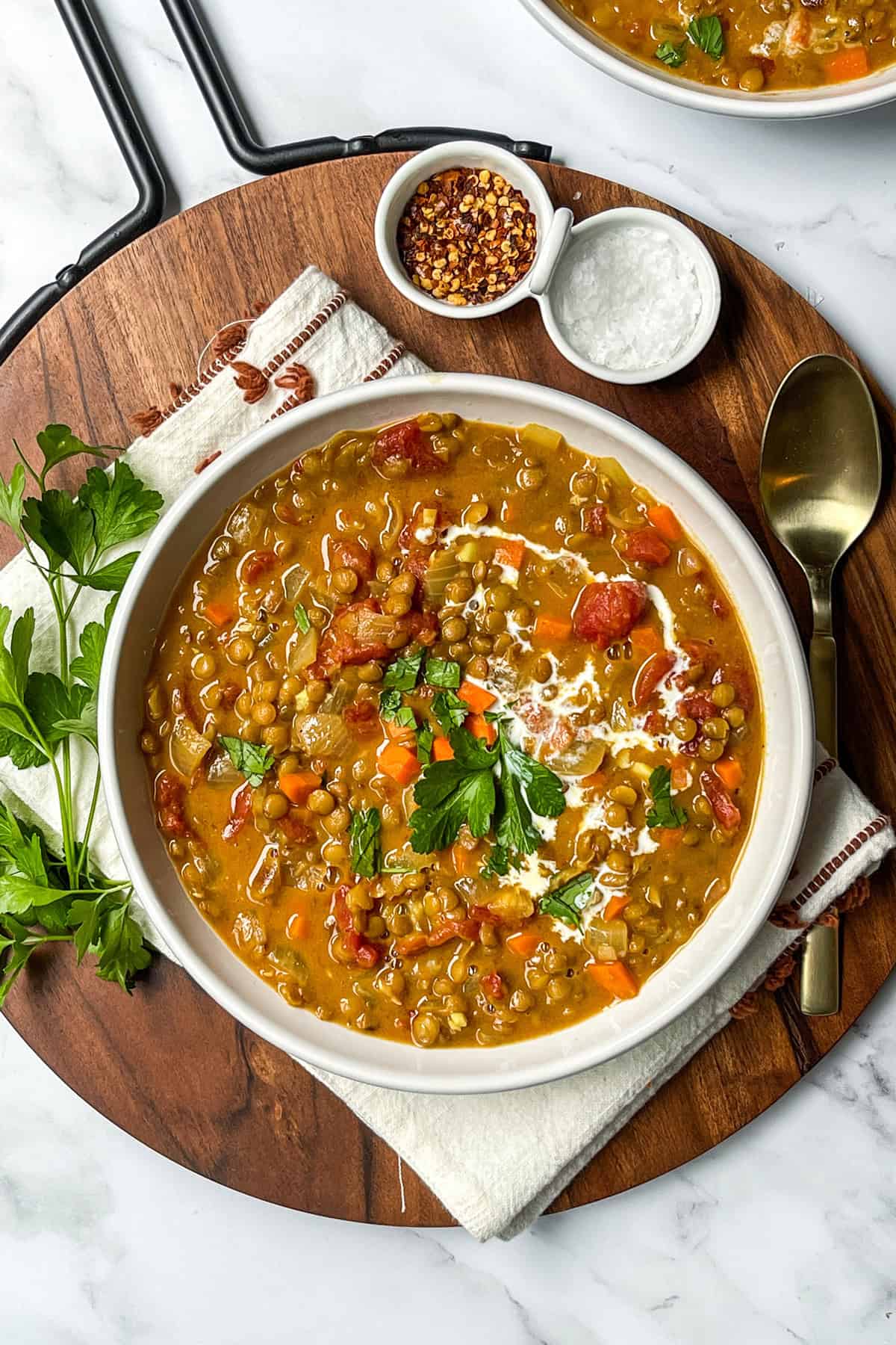 Bowl of curry lentil soup with coconut milk swirls and fresh herbs as garnish.