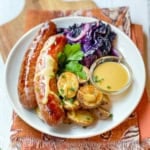 Sheet Pan Bratwurst, roasted potatoes, cabbage, and mustard sauce on a serving plate.