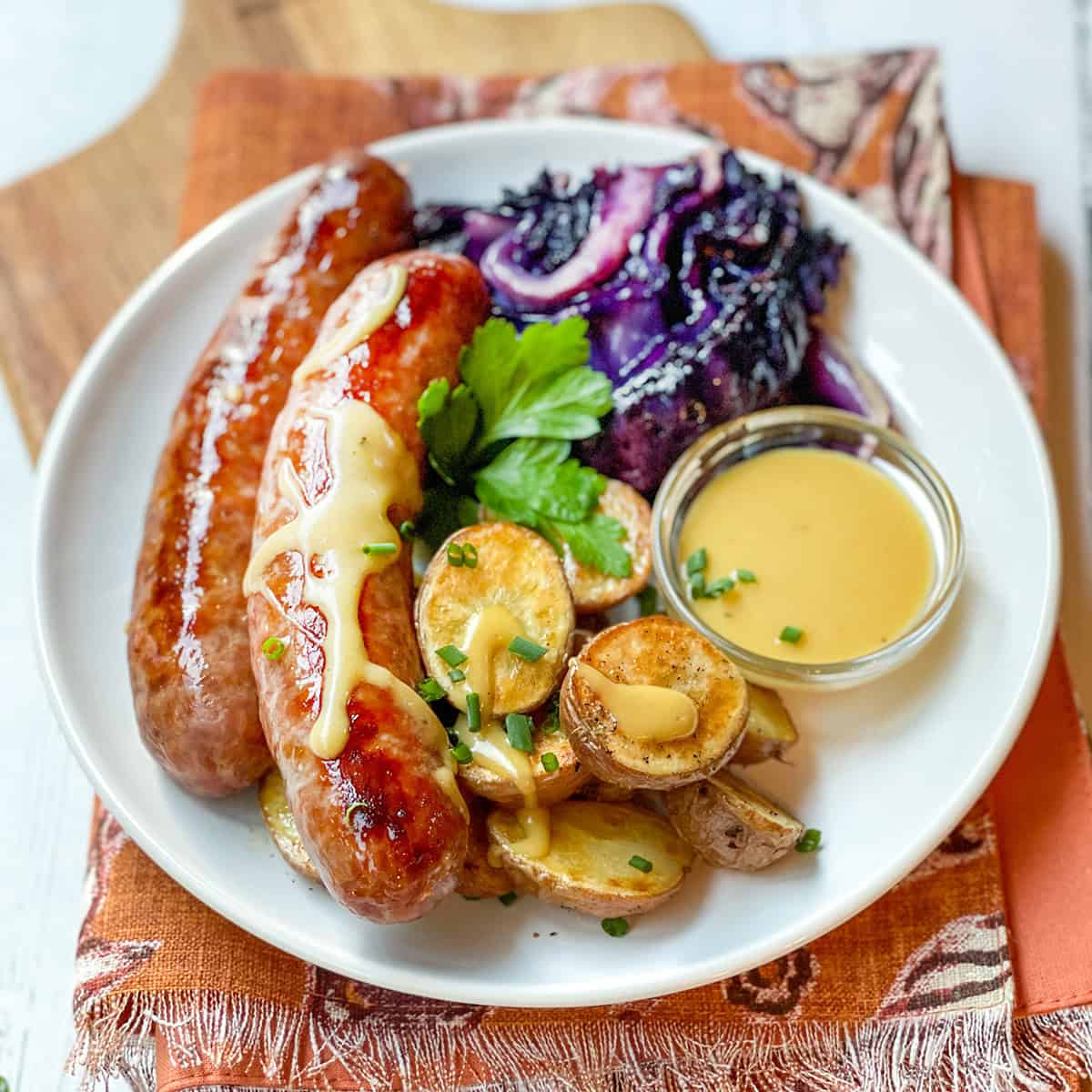 Sheet Pan Bratwurst, roasted potatoes, cabbage, and mustard sauce on a serving plate.