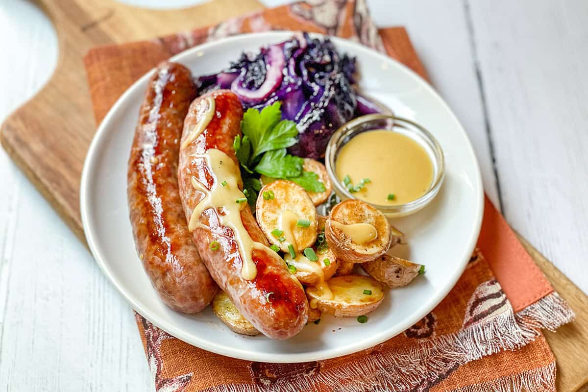 Sheet Pan German Bratwurst on a white plate with potatoes and red cabbage.