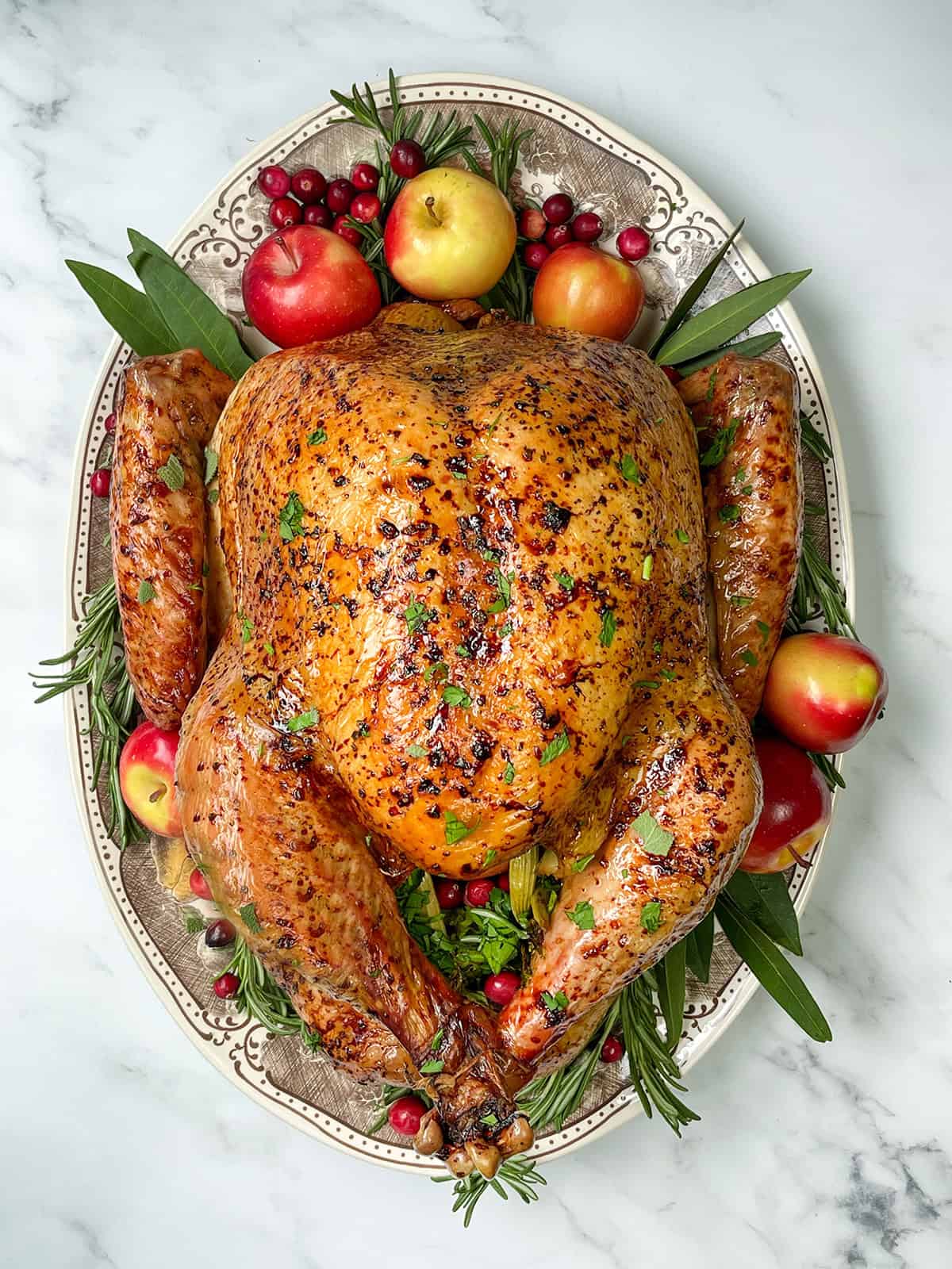 Top vertical view of apple cider roast turkey for the holidays garnished with fresh apples, bay leaves, rosemary and fresh cranberries on a serving platter.