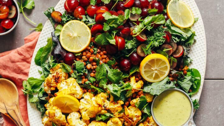 Top view of kale salad with grapes and curry roasted cauliflower in a white embellished serving platter.