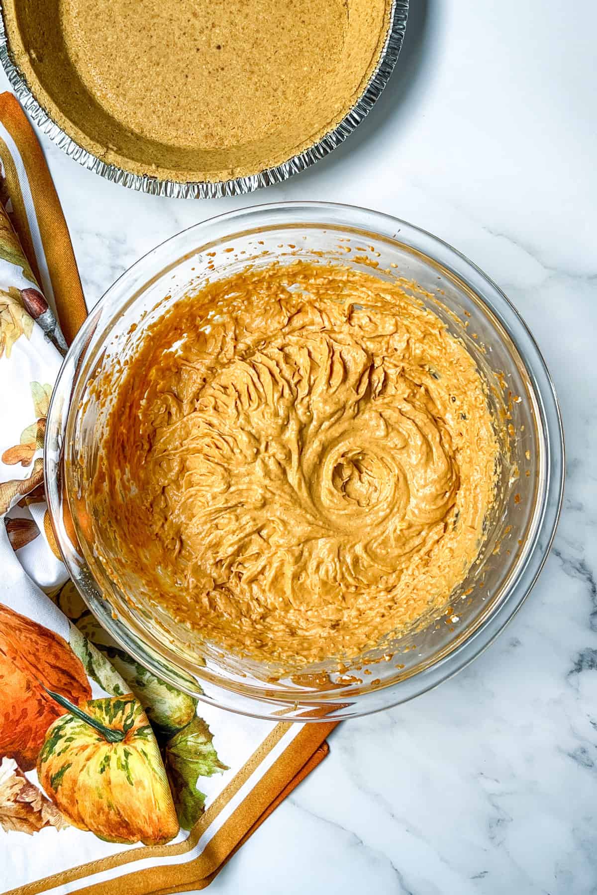 Pumpkin cheesecake filling mixture in glass bowl with graham cracker crust ready to fill.