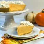 Slice of no bake pumpkin cheesecake with whipped cream and full pie in background.