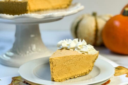 Slice of no bake pumpkin cheesecake with whipped cream and full pie in background.