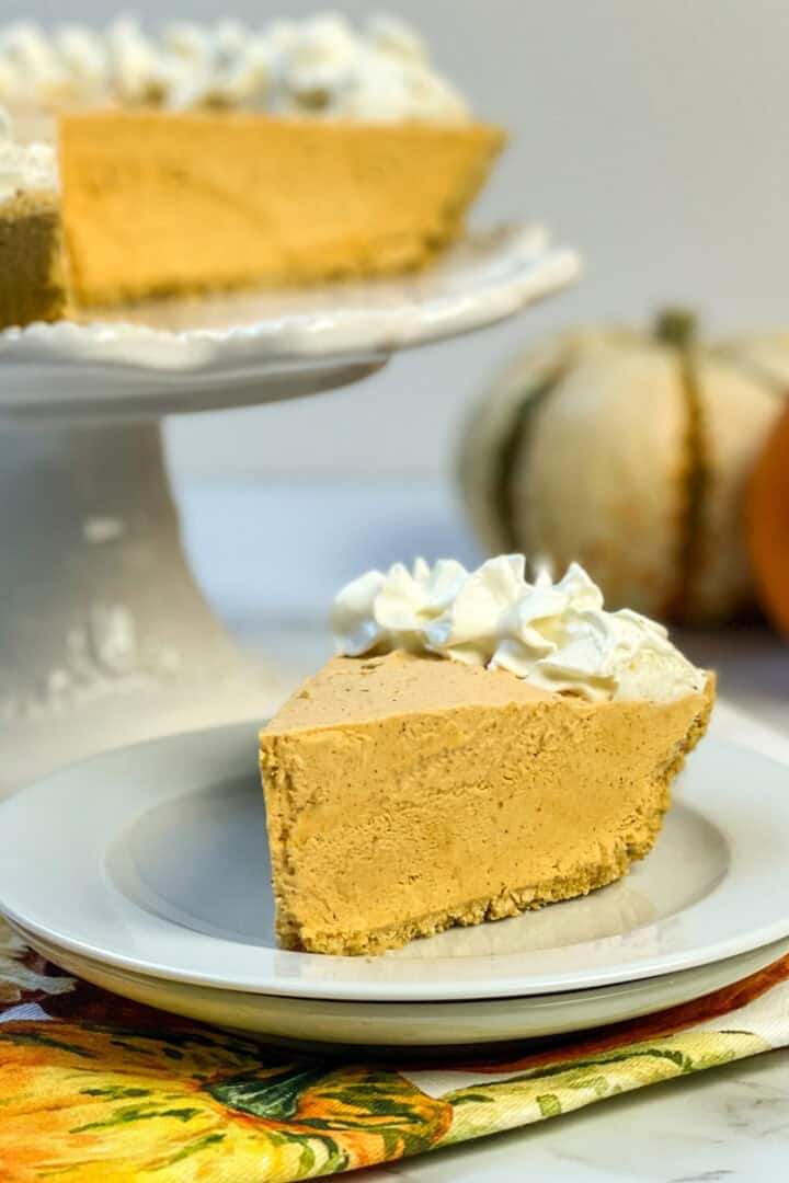 Slice of no bake pumpkin cheesecake with whipped cream and full pie in background.