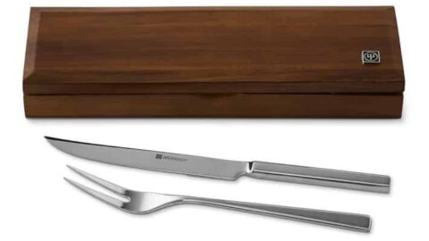 A stainless steel carving knife and fork set—Thanksgiving kitchen essential tools—are displayed next to a closed wooden storage box.