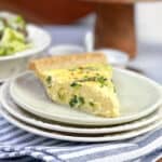 Slice of spinach quiche on a white plate, ready for serving, with a green salad in the background.