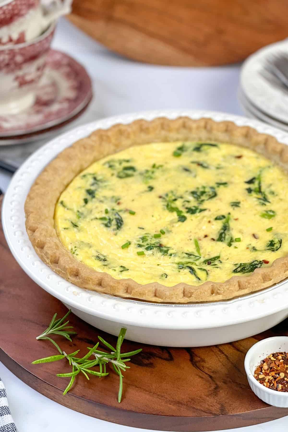 Unsliced spinach quiche in a quiche dish ready for slicing and serving.